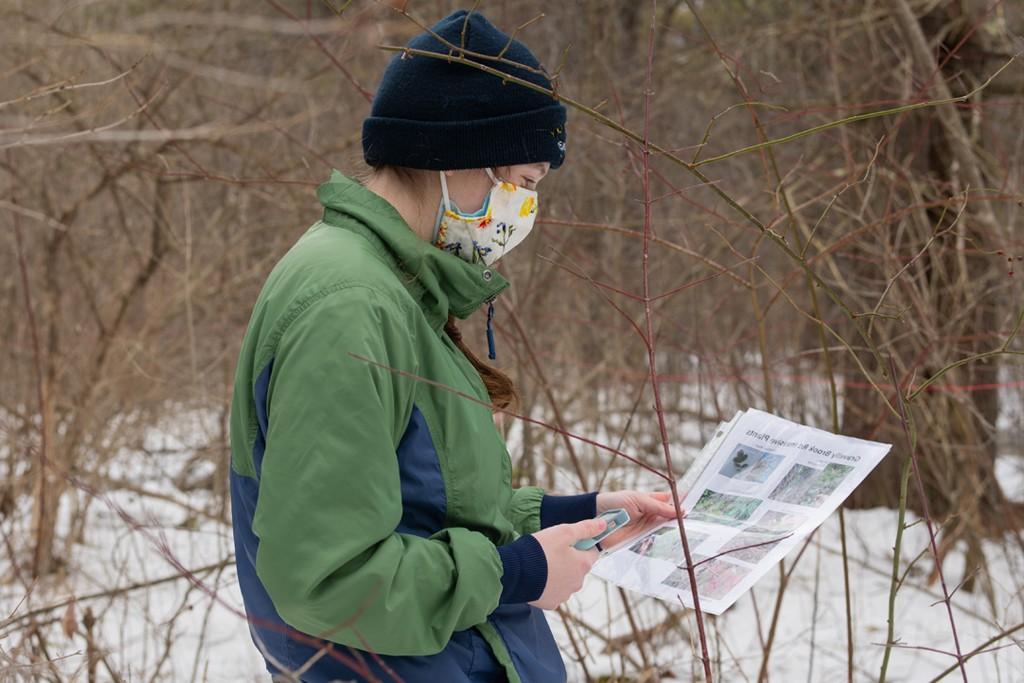 A student st和ing outside in the snow examines a informational flyer about birds