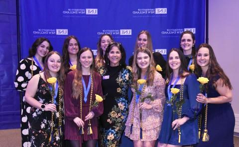 A group of students and faculty pose for a photo against a UNE-branded step-and-repeat